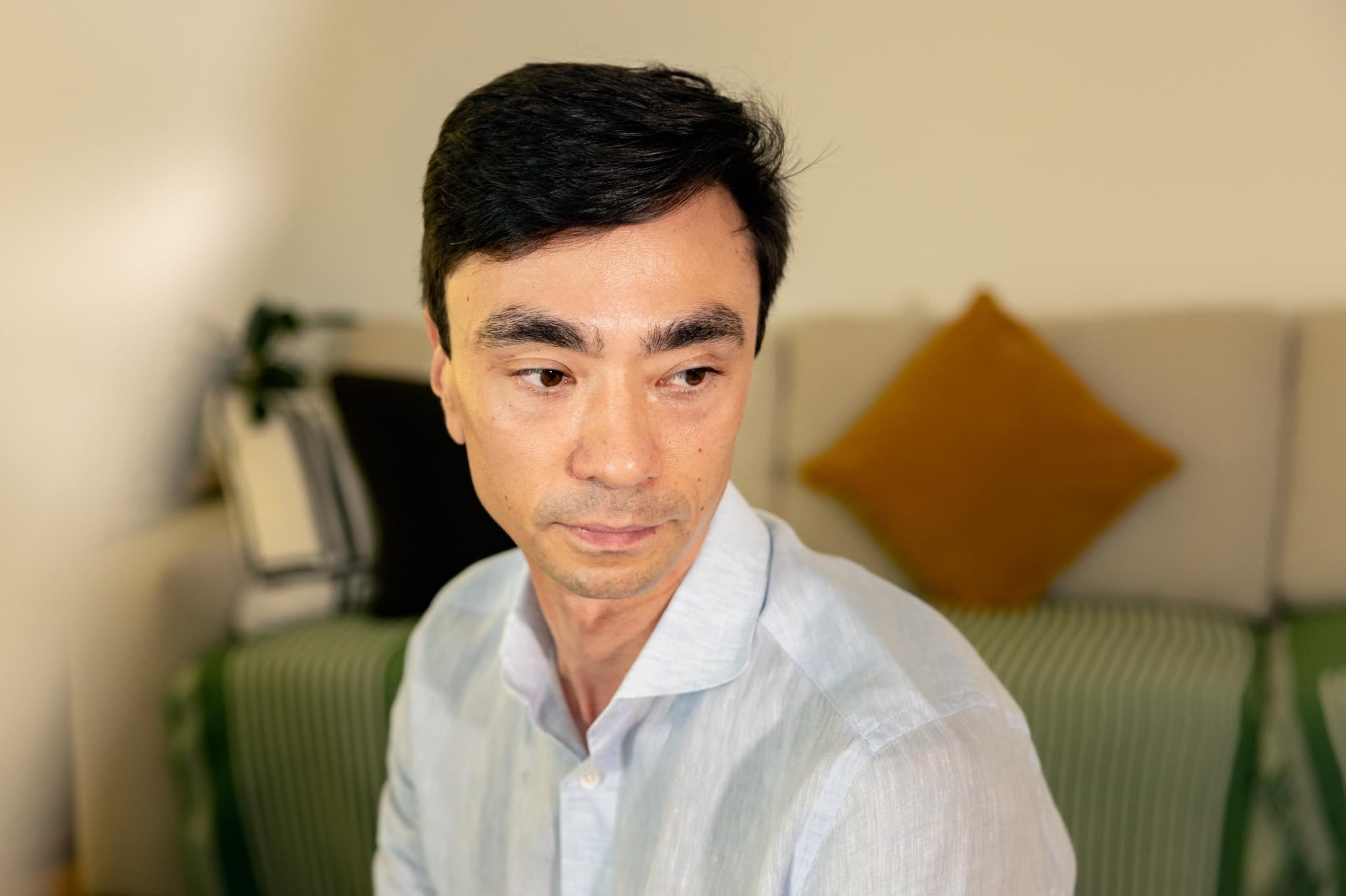 Alex Scott in a light blue shirt, seated on a green sofa