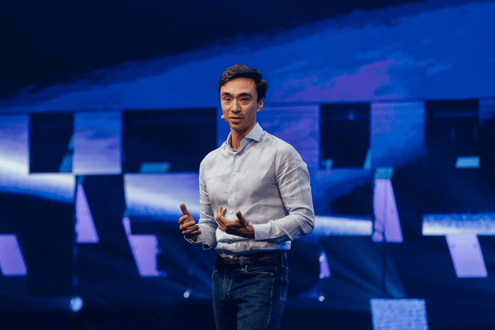 Alex Scott speaking on stage with a headset microphone